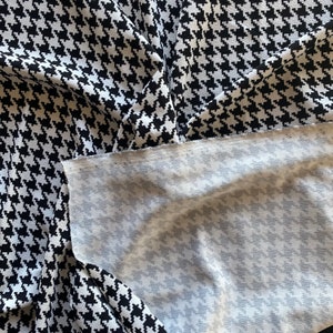 May include: Black and white houndstooth fabric with a white underside. The fabric is folded in half, showing both sides.