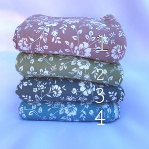May include: Four fabric swatches stacked on top of each other. The top swatch is a light pink with a white floral pattern. The second swatch is a light green with a white floral pattern. The third swatch is a dark green with a white floral pattern. The bottom swatch is a light blue with a white floral pattern. The swatches are numbered 1 through 4.