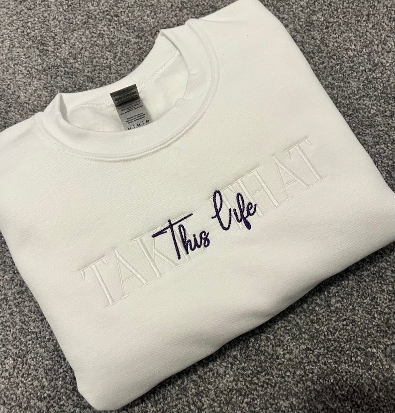 K&ouml;nnte beinhalten: Ein wei&szlig;es Sweatshirt mit dem gestickten Schriftzug "Take This life" in Marineblau und Wei&szlig;. Das Sweatshirt mit Rundhalsausschnitt ist aus weichem Material und f&uuml;r den l&auml;ssigen Gebrauch geeignet.