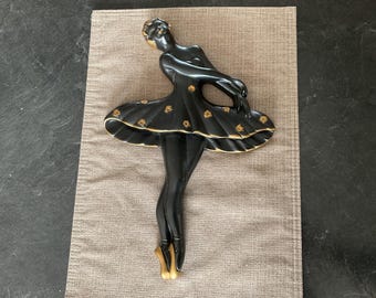 Peut inclure: Décoration murale de ballerine noire avec des accents dorés. La ballerine est en pose, les bras levés et la jupe qui s'échappe derrière elle.
