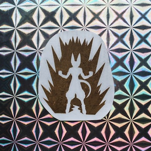 Könnte beinhalten: Ein weißer Aufkleber mit einer braunen Silhouette einer Figur mit einem Schwanz, die in einer Energieexplosion steht. Die Figur befindet sich in einer Kampfhaltung mit ausgestreckten Armen.