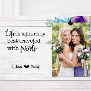 May include: A white wooden picture frame with a photo of two women hugging, holding bouquets. The frame has the text "Life is a journey best traveled with friends." and the names "Stephanie" and "Rachel".