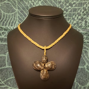 May include: A necklace with a braided cord and a pendant made of five dark brown seashells arranged in a flower shape.