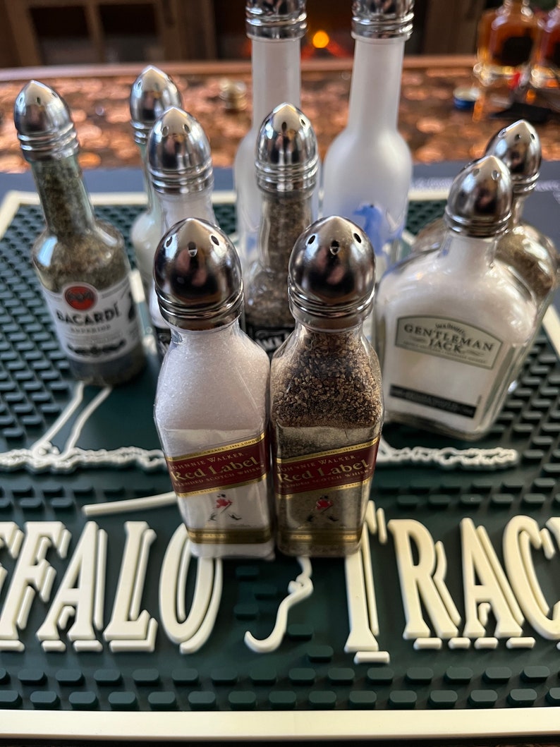 May include: A collection of miniature liquor bottles repurposed as salt and pepper shakers. The bottles are filled with various spices and labelled with brand names such as Bacardi, Gentleman Jack, and Johnnie Walker Red Label.