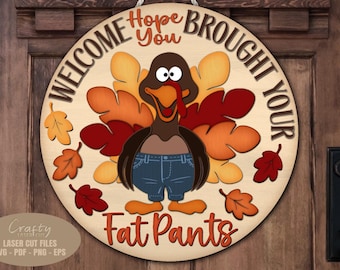 Könnte beinhalten: Runder Holzschild mit einer Truthahn-Cartoonfigur in Jeans. Der Schriftzug lautet "WELCOME, HOPE YOU BROUGHT YOUR FAT PANTS". Das Design umfasst Herbstblätter in Rot- und Orangetönen.