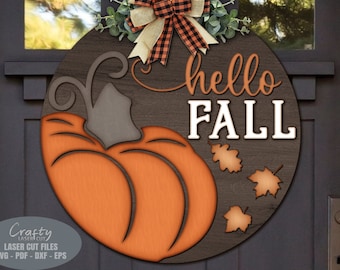 May include: A round wooden sign with a pumpkin and the text "hello fall" in white letters. The pumpkin is orange and has a brown stem. There are three brown leaves around the pumpkin.