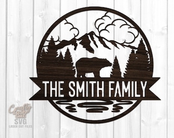 Puede incluir: Una silueta en blanco y negro de un oso, montañas, árboles y un lago en un círculo con el texto "THE SMITH FAMILY" en una pancarta debajo.