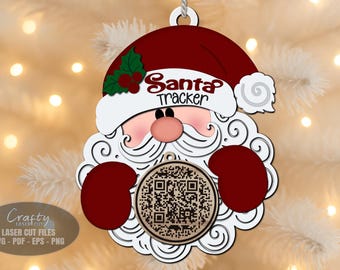 May include: A wooden Christmas ornament shaped like Santa Claus, featuring a red hat, white beard, and the text "Santa Tracker." The ornament includes a QR code and is designed with laser-cut details. The ornament is hanging from a white string.