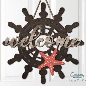 Könnte beinhalten: Ein hölzernes Willkommensschild mit nautischem Thema. Das Schild zeigt ein Schiffssteuerrad mit einem daran hängenden Seestern. Das Schild sagt "welcome" in einer kursivschrift.