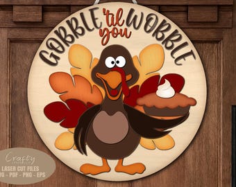 May include: Round wooden sign with a cartoon turkey holding a pie. The sign has the text "Gobble 'til you Wobble" in black and red. The turkey is brown, orange, and yellow.