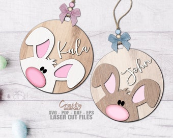 May include: Two wooden Easter bunny ornaments with pink ears and noses. The ornament on the left has a white bunny with the name "Kala" written on it. The ornament on the right has a brown bunny with the name "John" written on it.