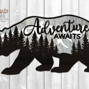 May include: Black silhouette of a bear with a mountain range and pine trees inside the bear's outline. The text "Adventure Awaits" is written in a cursive font above the trees.