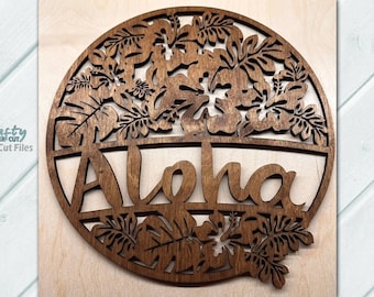 May include: A brown wooden circle with a cut-out design of tropical leaves and flowers. The word "Aloha" is cut out in the centre of the circle.