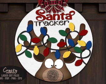 May include: A round wooden Christmas sign with a reindeer design. The sign reads "Santa Tracker" in red script. The reindeer has brown antlers adorned with colorful Christmas lights. A red and black plaid bow tops the sign.