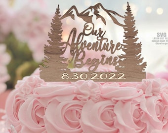 May include: Wooden cake topper featuring a mountain range, two pine trees, and the text "Our Adventure Begins 8.30.2022".