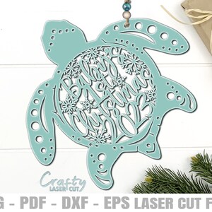Può includere: Ornamento a forma di tartaruga in legno tagliato al laser, color verde acqua chiaro, con le parole "Baby Christmas 2023" e dettagli a fiocco di neve. L'ornamento è appeso a un filo. L'immagine include anche il testo "Crafty Laser Cut".