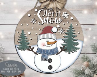 May include: A round wooden sign with a snowman and the text "Let it Snow" in white. The snowman is wearing a red and white hat, a blue scarf, and has a carrot nose. There are two green pine trees on either side of the snowman.