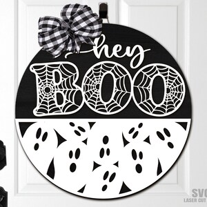Puede incluir: Un colgador de puerta redondo en blanco y negro con el texto "They Boo" en un diseño de telaraña blanca. La mitad inferior del colgador presenta un diseño de fantasma blanco con ojos negros.