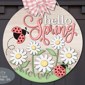 Puede incluir: Un letrero redondo de madera con las palabras "hello Spring" en blanco y rosa. El letrero presenta margaritas, mariquitas y un lazo de cuadros. El letrero está diseñado para la decoración de primavera.
