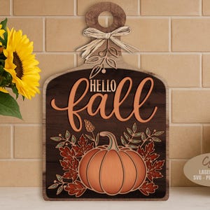 May include: Wooden fall-themed sign with a pumpkin and the words "Hello Fall." The sign is brown with orange lettering and accents. A decorative bow and leaves are at the top. A vase of sunflowers is to the left.