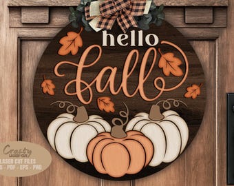 May include: A round wooden sign with the words "hello Fall" in white and orange script. The sign features three pumpkins and fall leaves. A decorative bow and greenery are at the top. The sign is hanging on a wooden door.