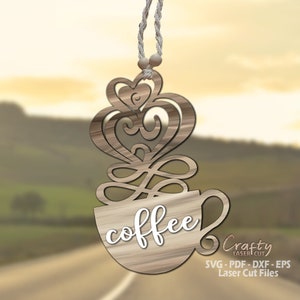 Könnte beinhalten: Ein Holz-Kaffeebecher-Anhänger mit einem dekorativen herzförmigen Dampfdesign. Der Becher hat das Wort "coffee" darauf geschrieben. Der Anhänger hängt an einer Schnur.
