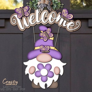 May include: Purple gnome with a white beard and a purple flower on its chest. The gnome is wearing a purple hat with yellow trim and butterflies. The gnome is hanging from a wooden sign that says "Welcome".