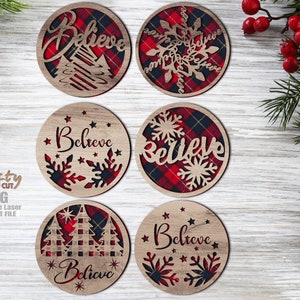 Può includere: Sei ornamenti rotondi in legno con un motivo a quadri rosso e nero. Ogni ornamento presenta un design diverso, tra cui fiocchi di neve, alberi di Natale e la parola "Believe".