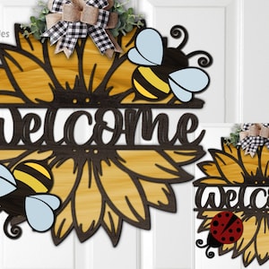 May include: A wooden welcome sign with a sunflower design. The sunflower has a wood grain texture and is surrounded by two bees. The word "welcome" is written in a black script font.