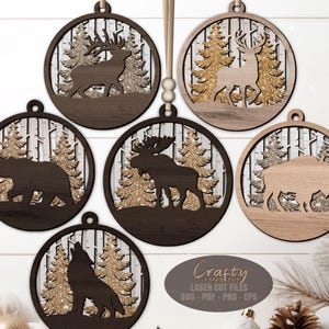 May include: Six wooden Christmas decorations with laser-cut wildlife silhouettes. Each ornament features a different animal: a deer, bear, moose, bison, and wolf, set against a backdrop of trees. The decorations are round with a hanging loop.