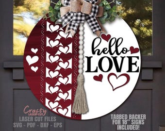 May include: A round wooden sign with a white background and a red background. The white side says "hello LOVE" in black lettering with a red heart. The red side has a pattern of white hearts. A white beaded garland with a brown tassel hangs from the top.