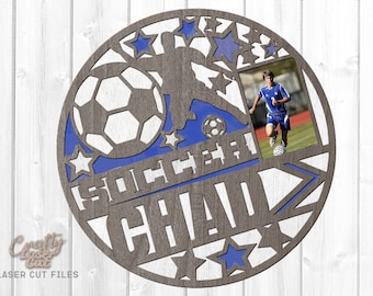May include: A grey wooden circle with a blue and white football design. The circle has a cutout for a photo and the words "Soccer Chad" are written on it.