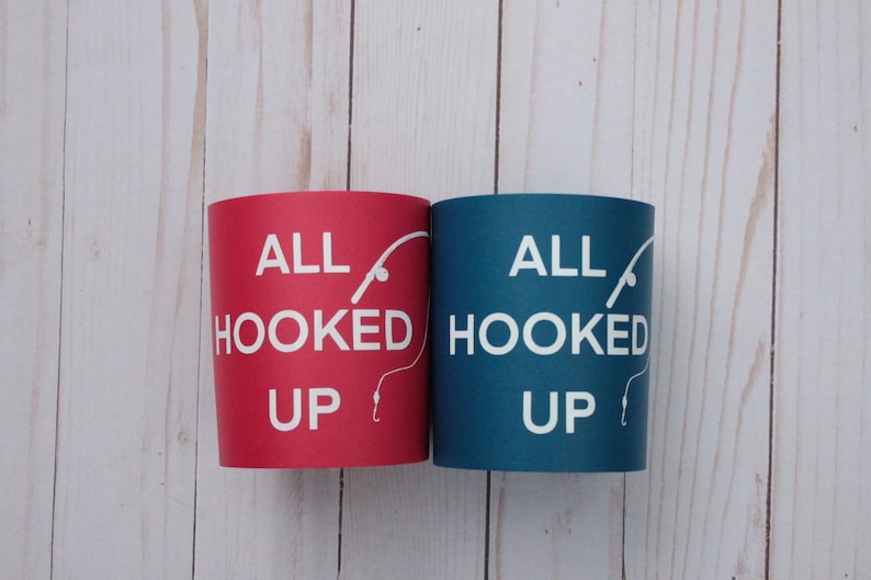 Puede incluir: Dos enfriadores de latas, uno rojo y otro azul, con el texto "All Hooked Up" y un gr&aacute;fico de ca&ntilde;a de pescar y anzuelo.