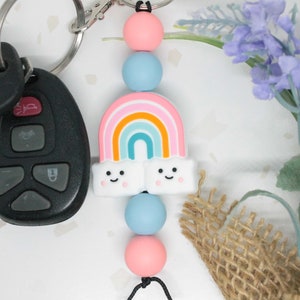 May include: A rainbow-themed keychain with a rainbow, clouds, and colorful beads. The keychain is attached to a silver key ring.