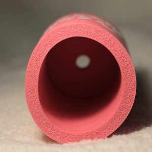 Puede incluir: Un cilindro de espuma rosa con un agujero en el centro. La espuma tiene una superficie texturizada.