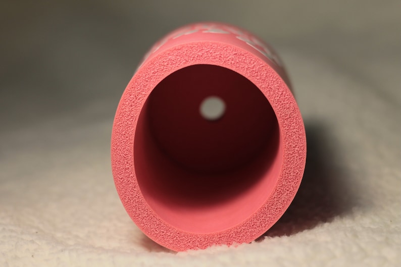 Puede incluir: Un cilindro de espuma rosa con un agujero en el centro. La espuma tiene una superficie texturizada.