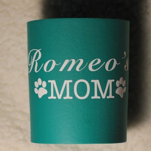 Puede incluir: Taza aislante azul turquesa con texto blanco que dice "Romeo's MOM" con dos huellas de patas blancas a cada lado de la palabra MOM.