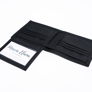 May include: A black trifold wallet with a clear plastic window on the front. The window displays a business card that reads "Maria Elova Designs Handmade Bags for Women, Men & Kids!"