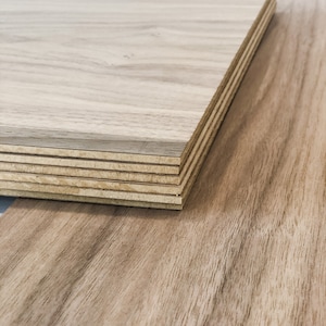 May include: A stack of wood veneer sheets, showing the layers of plywood. The top sheet has a light brown wood grain pattern.