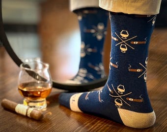 Puede incluir: Calcetines azul marino con un estampado de puros y vasos de whisky. Los calcetines tienen talón y puntera beis. Un puro y un vaso de whisky están sobre una superficie de madera.