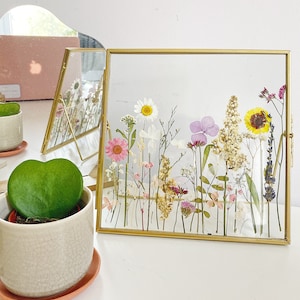 Personalisierter botanischer getrockneter gepresster Blumenrahmen, der Goldfoto-Wandbehang steht |