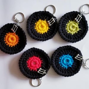 May include: Five crocheted black vinyl record keychains with different colored centers. Each keychain has a silver music note charm attached.