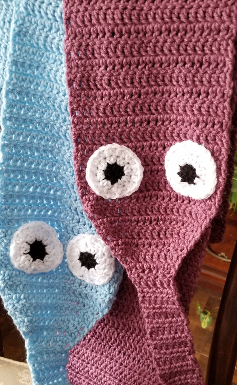 May include: A crocheted blanket with a blue and burgundy color scheme. The blanket has a pattern of eyes crocheted on it.