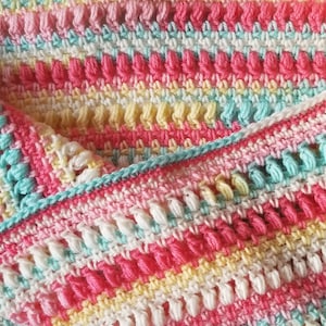 May include: A colorful crocheted baby blanket with a textured stitch pattern in shades of pink, yellow, blue, and white.