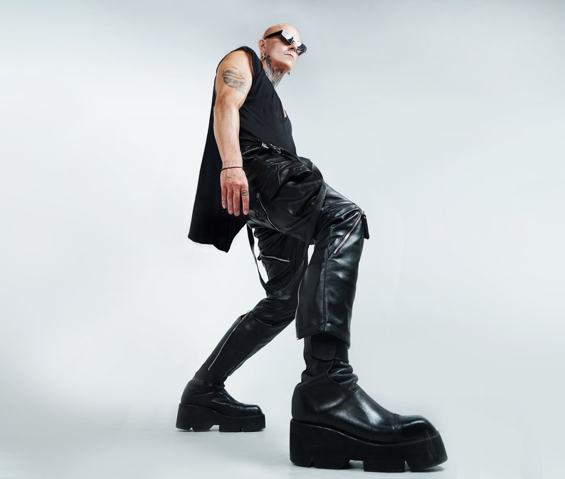 K&ouml;nnte beinhalten: Eine Person tr&auml;gt ein schwarzes Tanktop, eine schwarze Lederhose und schwarze Stiefel. Die Person hat einen rasierten Kopf und tr&auml;gt eine Sonnenbrille.