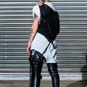 May include: A person with yellow hair wearing a white t-shirt, black leather pants, and black high-top sneakers. They are carrying a black leather backpack.
