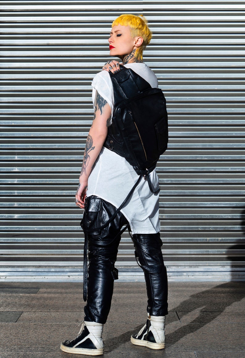 May include: A person with yellow hair wearing a white t-shirt, black leather pants, and black high-top sneakers. They are carrying a black leather backpack.