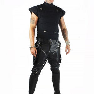 K&ouml;nnte beinhalten: Eine Person tr&auml;gt ein schwarzes Shirt mit Stehkragen, eine schwarze Lederhose mit Rei&szlig;verschlussdetails und schwarze Stiefel. Sie tr&auml;gt auch eine schwarze M&uuml;tze und eine Sonnenbrille.