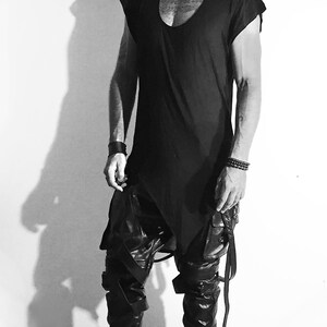 May include: A black sleeveless shirt with a scoop neck and a long, asymmetrical hem. The shirt is paired with black leather pants and black combat boots.