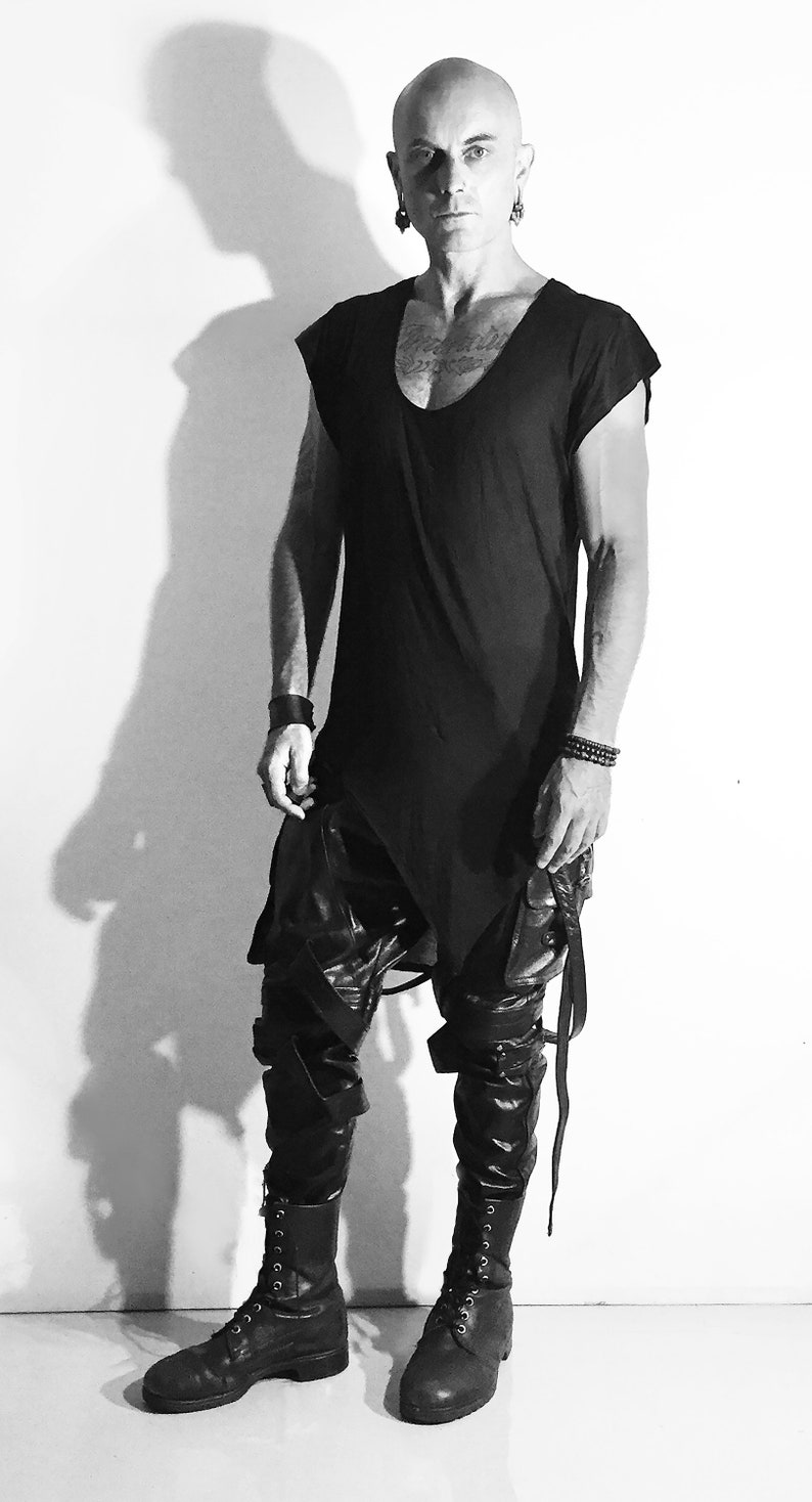 May include: A black sleeveless shirt with a scoop neck and a long, asymmetrical hem. The shirt is paired with black leather pants and black combat boots.